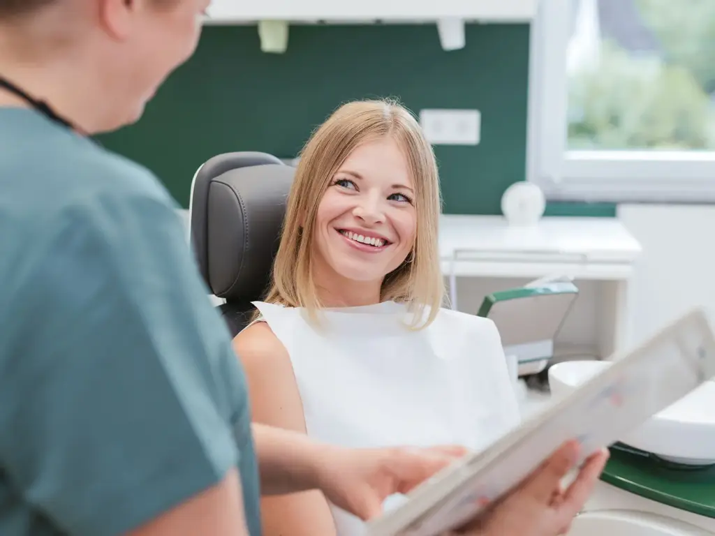 Patientin lächelt im Behandlungsstuhl, Beratung durch Zahnarzt